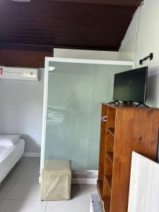 a room with a tv on a wooden dresser with a bed and a tv at Apartamentos Aconchegantes, Villa da Praia in Praia do Forte