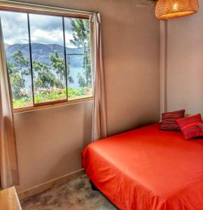 1 dormitorio con cama roja y ventana en Linda Casa de campo frente a Laguna de Pacucha, en Pacucha