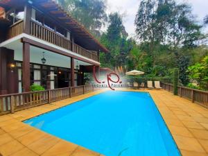 a blue swimming pool in front of a house at Pousada Demuner's House - Espaço Aconchegante Itaipava in Petrópolis