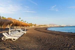 a row of lounge chairs on a beach with a straw umbrella at Apartamento Bungamerica 2 bedrooms Costa Adeje in Playa de las Americas