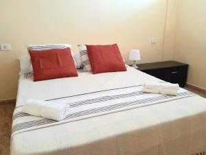 ein großes weißes Bett mit zwei roten Kissen darauf in der Unterkunft Perfectly located apartment with pool in Playa de las Americas + 13 Fotos