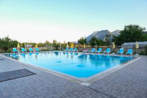 a large swimming pool with blue chairs and mountains in the background at Apella Hotel in Cıralı