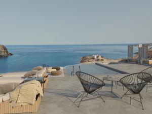 een patio met stoelen en tafels en uitzicht op het water bij Mykonos Residence Villas & Suites Merchia Beach in Merchia Beach