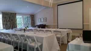 une salle de conférence avec des tables et des chaises blanches et un écran dans l'établissement 18 Pioneer Kloof, à Kloof