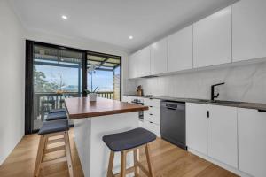 a kitchen with white cabinets and a counter with stools at The Woodpecker in Merimbula