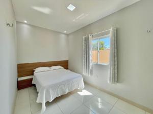a white bedroom with a bed and a window at Pousada Beach House Dunas in Beberibe