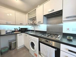 cocina con armarios blancos, lavadora y secadora en Genesis 3 bedroom Home Telford- sleeps up to 5 en Oakengates