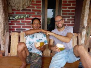 two men sitting on a bench holding drinks at Gado-gado BnB in Yogyakarta