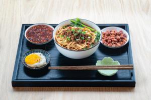 a tray with a bowl of noodles and other bowls of food at Wuyu Hotel - Chongqing Liangjiang Happiness Plaza in Chongqing