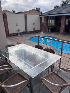una mesa de cristal y sillas en un patio con piscina en Beverley Grove Guest House en Gqeberha