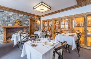 a restaurant with white tables and chairs and a stone wall at Hôtel Les Peupliers in Courchevel