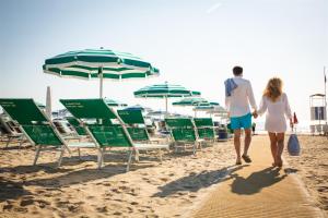 una coppia che cammina lungo la spiaggia con sedie e ombrelloni di Don Antonio Glamping Village a Giulianova