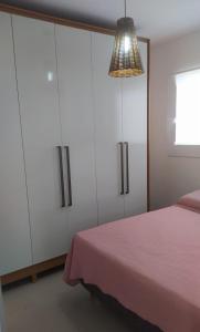 a bedroom with white cabinets and a pink bed at Apartamento aconchegante em Itajaí in Itajaí