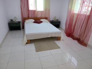 1 dormitorio con 1 cama con cortinas rojas y suelo blanco en Maison rénovée à Itaosy Cité Akany Sambatra, en Antananarivo