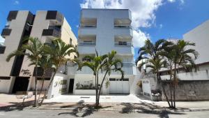 Lindo apartamento com Wi-Fi a 370m da Praia do Morro, próximo ao Marlim Azul e à Av Paris في غواراباري: مبنى ابيض امامه اشجار النخيل