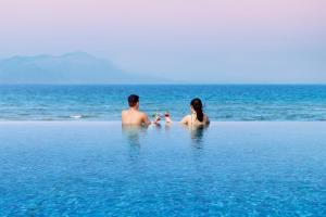 a man and woman sitting in the water on a beach at Melia Danang Beach Resort in Da Nang