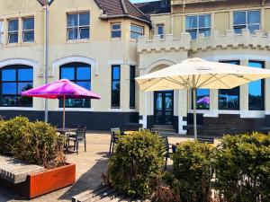 deux parasols, tables et chaises devant un bâtiment dans l'établissement The Grand Hotel, à Port Talbot