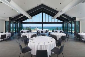 um salão de banquetes com mesas e cadeiras brancas e janelas grandes em Hilton Garden Inn Busselton em Busselton