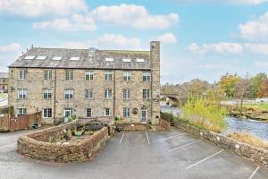 an old brick building with a river in front of it at Bridge End Mill Holiday Apartments in Settle
