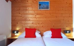 Cette chambre dispose de 2 lits avec des oreillers rouges et de murs en bois. dans l'établissement Hotel Emeraude, à Peisey-Nancroix