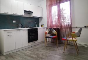 una cocina con armarios blancos y 2 sillas en Nikos Residence, en Roman