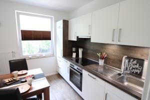cocina con armarios blancos, fregadero y mesa en Appartementhaus-Kogge-Wohnung-10 en Cuxhaven