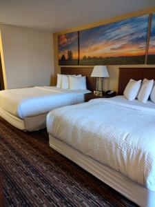 two beds in a hotel room with a painting on the wall at Days Inn & Suites by Wyndham Fargo 19th Ave/Airport Dome in Fargo