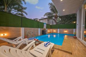 a swimming pool with white lounge chairs and a house at Elegant Villa By Tropicana Stays in Lonavala