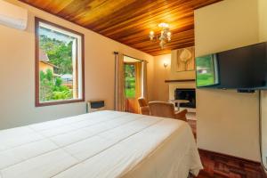 een slaapkamer met een groot wit bed en een televisie bij Pousada Serra Villena in Monte Verde