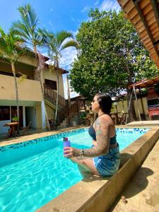 a woman sitting next to a swimming pool with a drink at Pousada JK in Pirenópolis