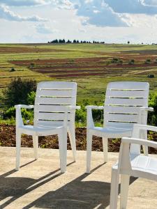 two white chairs sitting on a patio with a field at Cozy Farm 3BDRM 8 km ThabaBosiu in Maseru