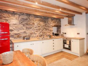 - une cuisine avec des placards blancs et un mur en pierre dans l'établissement Bull Bach Old Smithy, à Pwllheli