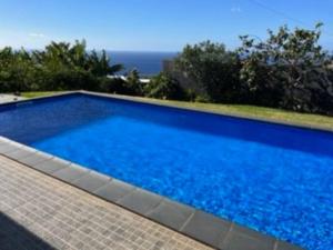 a large blue swimming pool with the ocean in the background at Moradia com piscina no Caniço in Caniço