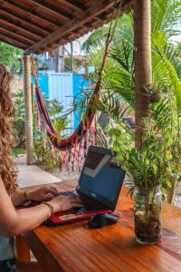 Back to the Beach Hostel - Pipa في بيبا: امرأة تجلس على طاولة خشبية مع جهاز كمبيوتر محمول