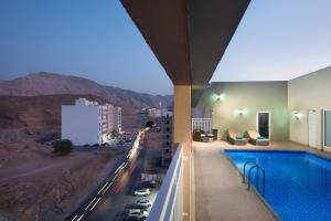 a building with a swimming pool and a view of a city at Centara Life Muscat Dunes Hotel in Muscat