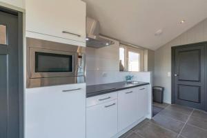 a kitchen with white cabinets and a microwave at NEW! Strandhuis 't Koepeltje aan zee! in Callantsoog