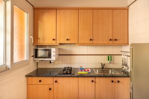a kitchen with wooden cabinets and a sink and a microwave at Albamar Apartaments in Lloret de Mar
