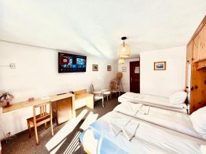 Habitación con 3 camas y TV en la pared. en Hotel Old JNN, en Klosters Serneus