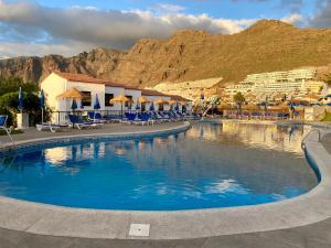 a swimming pool with chairs and mountains in the background at Seaview Townhouse in Puerto Santiago & Los Gigantes in Puerto de Santiago