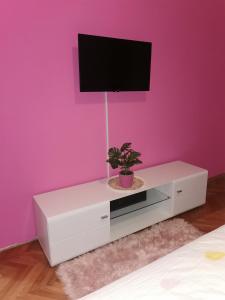a white dresser with a tv on a pink wall at Apartman Aki in Pirot