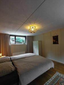 een slaapkamer met een groot bed en een kroonluchter bij Luxe familiehuis 8p nabij bos en hei op de Veluwe in Putten