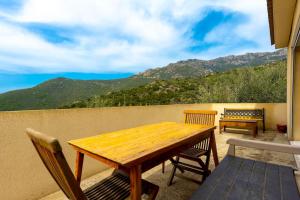 einen Holztisch und Stühle auf einem Balkon mit Bergblick in der Unterkunft SEJOUR DETENTE BALAGNE ENTRE MER ET MONTAGNE in Urtaca