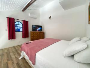 um quarto com uma cama branca com cortinas vermelhas e uma televisão em Villas & Residencial Três Marias à 300 mts do Centro Histórico Paraty em Paraty