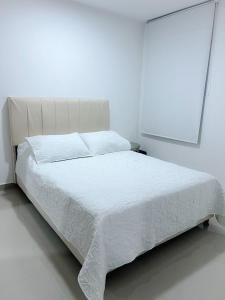un letto bianco in una camera da letto bianca con copriletto bianco di Apartaestudio Amoblado a Valledupar