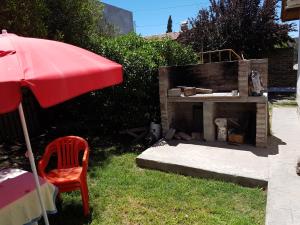 a brick fireplace with a red umbrella and a chair at Casa con pileta "TU CASITA EN VIEDMA" calle Junin 1877 in Viedma