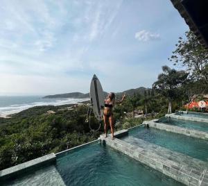 a woman standing next to a swimming pool with a surfboard at Pousada Rosa Norte in Imbituba
