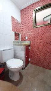 een badkamer met een toilet en een rode betegelde muur bij Apartamento a Duas Quadras da Praia in Cabo Frio