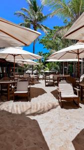 uma praia arenosa com mesas, cadeiras e guarda-sóis em Pousada Villa Zena - Pé na areia em Arraial d'Ajuda