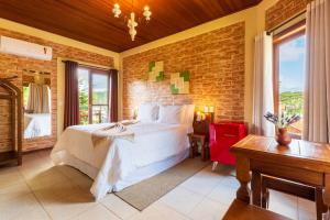 a bedroom with a white bed and a brick wall at Pousada Boutique Vilage de Minas in Monte Verde