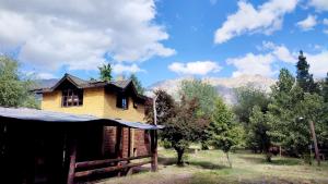 een houten huis in een veld met bomen en bergen bij Hostel,Dormis y Camping Costa Bolsón in El Bolsón